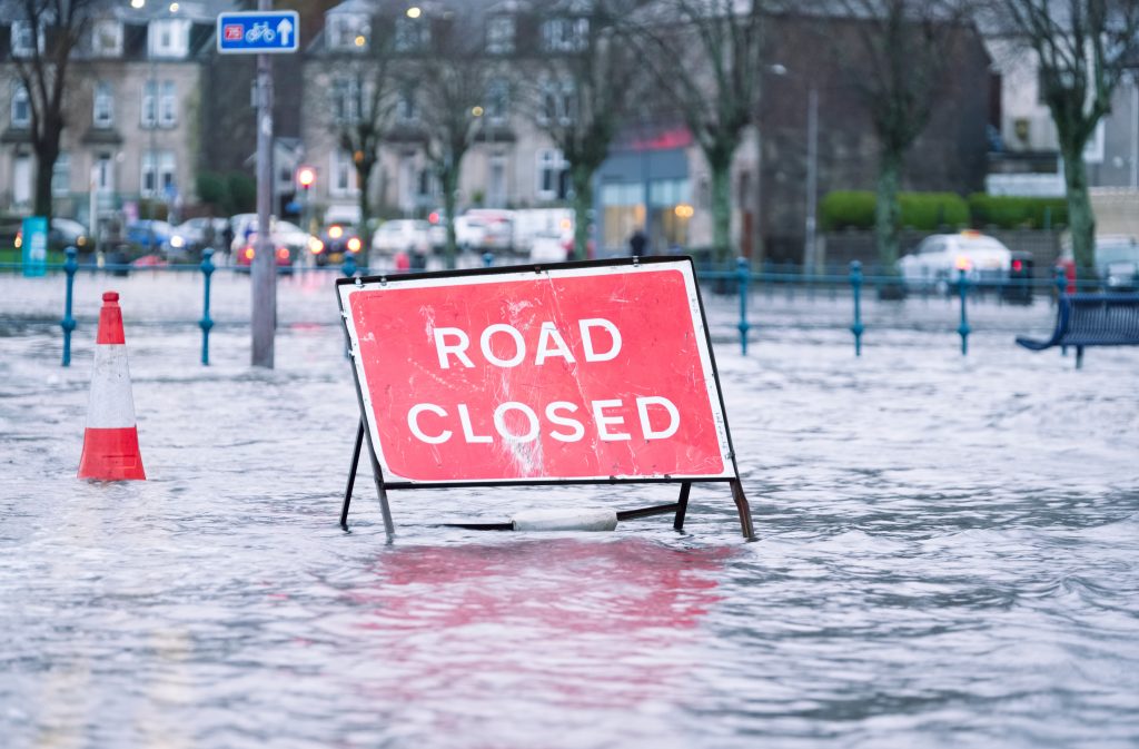 intense rain storms causing major challenges for rainwater disposal: Road Closed sign in water where a road would have been before flooding occured